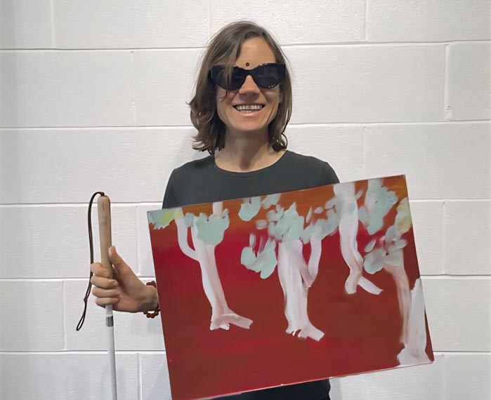 Juliet Jackson holds her white cane and one of her paintings